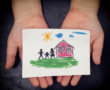 Child holds a drawn house with family